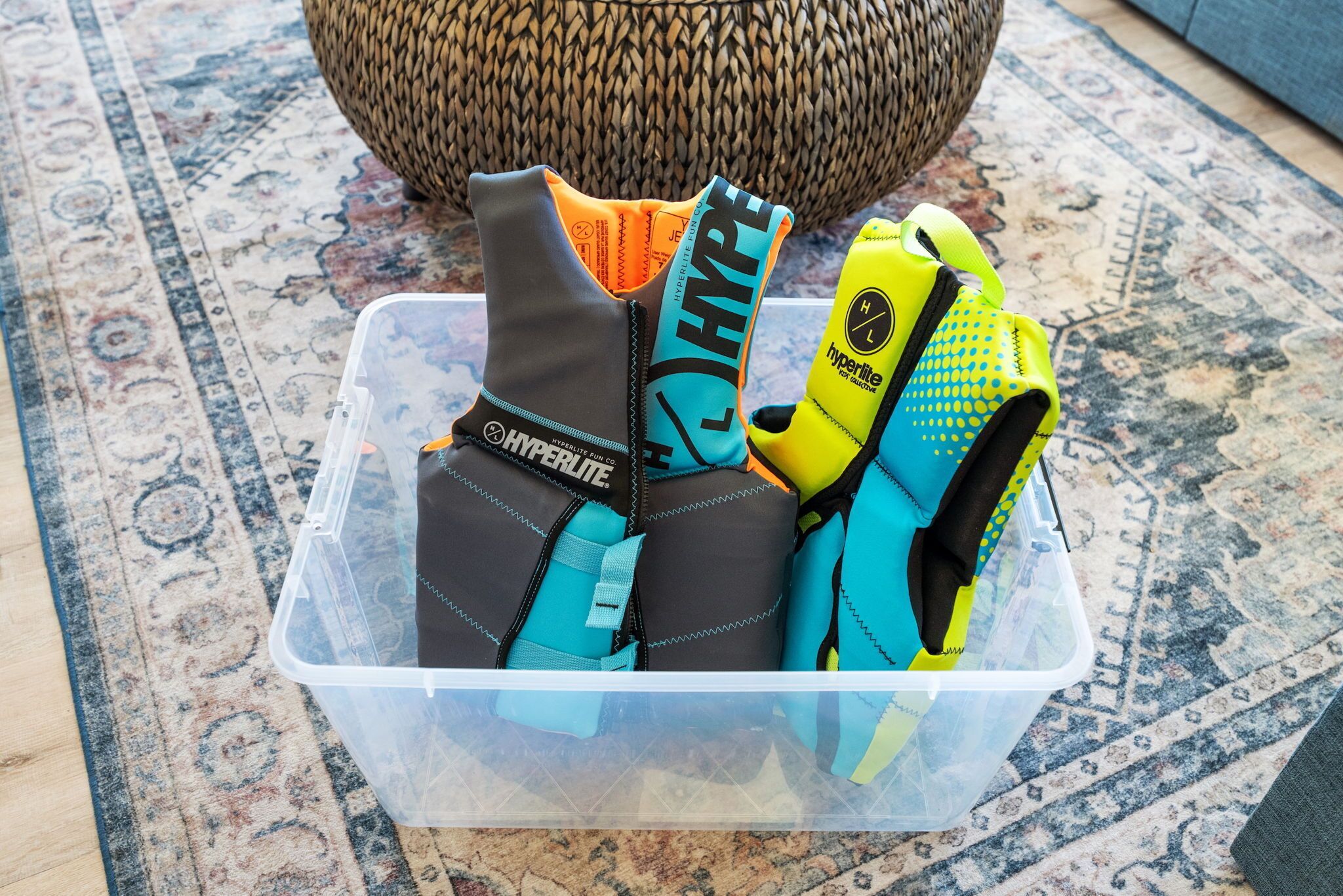 A plastic container with several pairs of gloves, including 'Hyperlite' and 'HYPE' branded gloves, on a patterned rug.