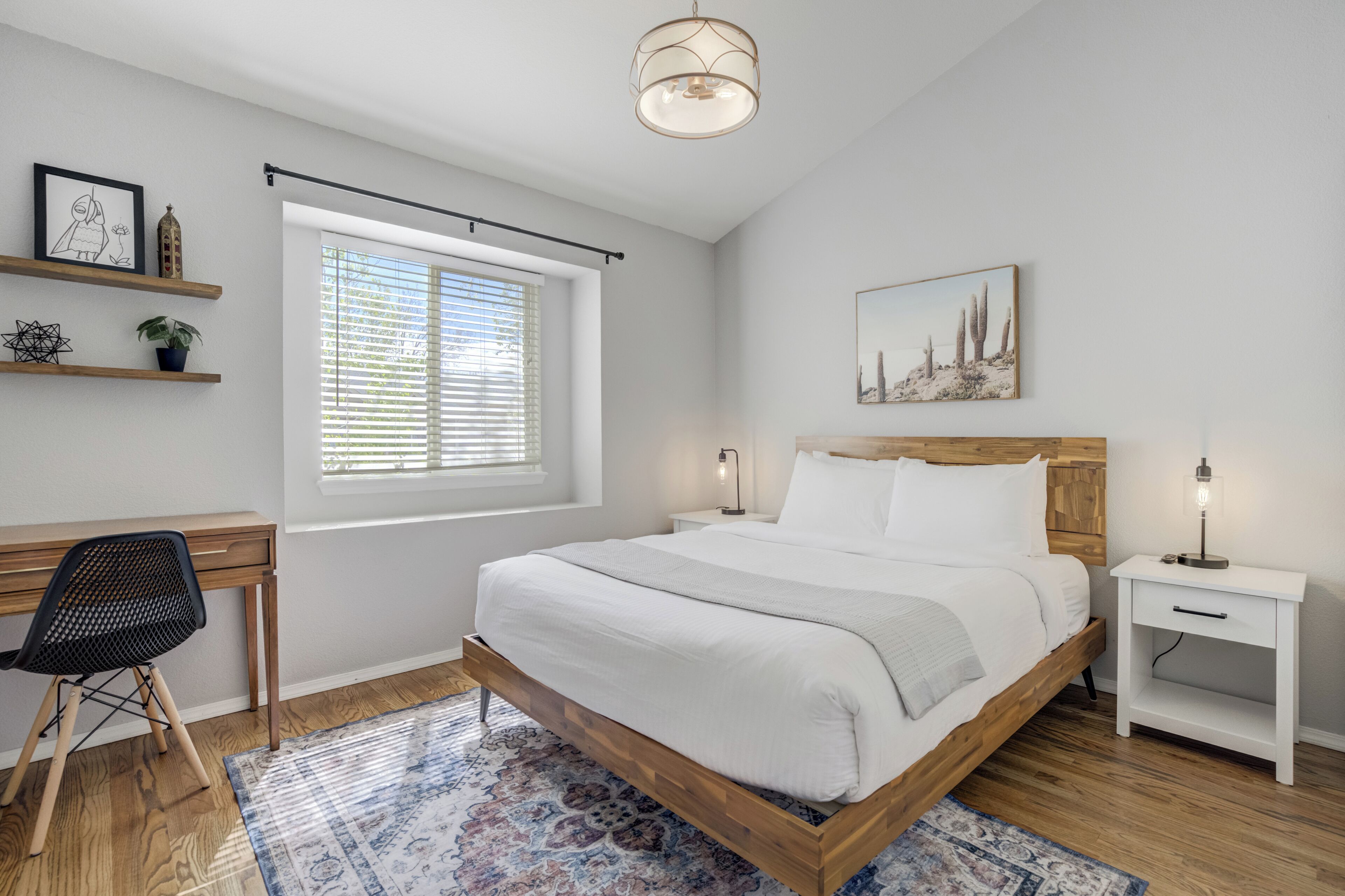 Une chambre à coucher avec un lit en bois, un bureau, une chaise, une table de chevet et une fenêtre avec des stores.