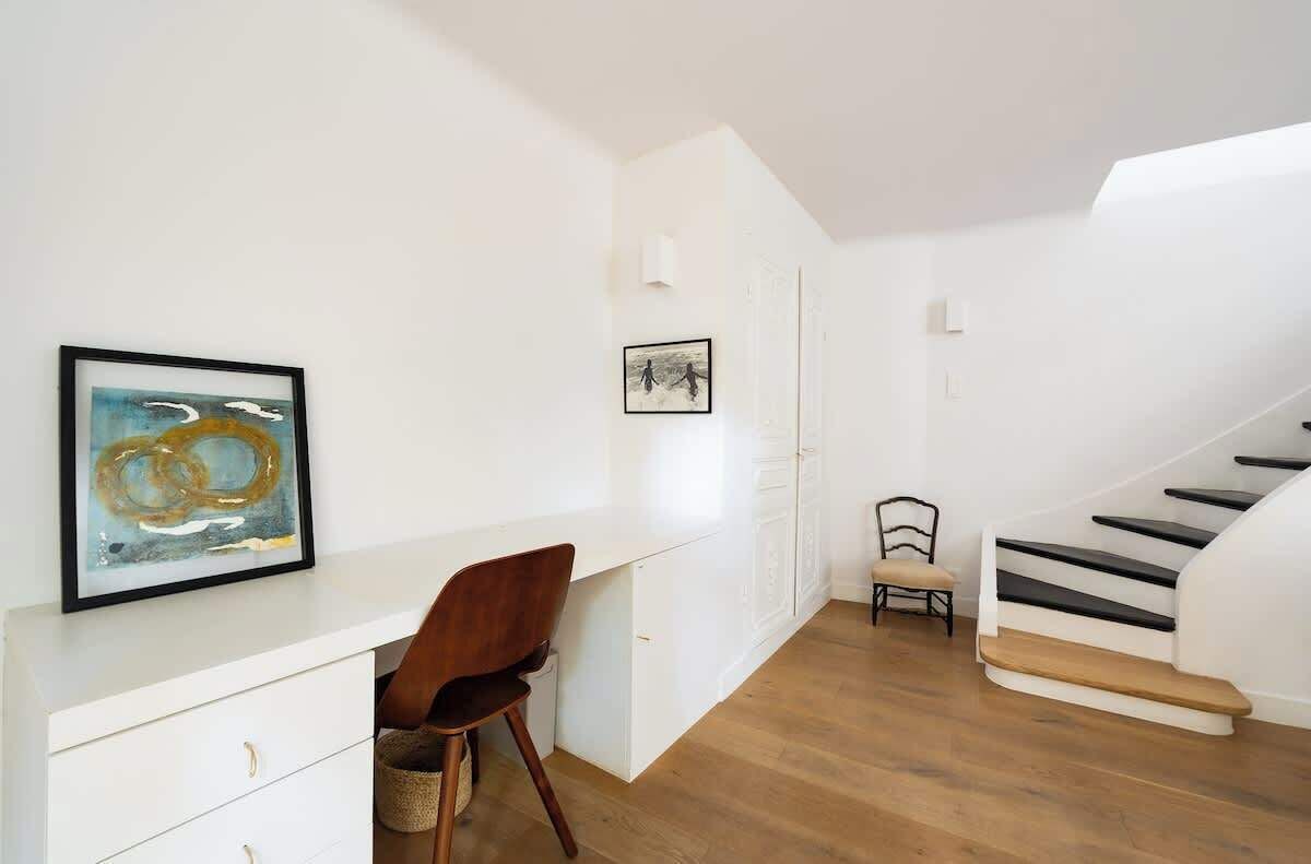 Ein modernes Interieur mit einem weißen Schreibtisch, einem Stuhl, einer Treppe und Kunstwerken an den Wänden.