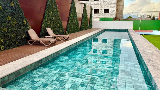 Una piscina con suelo de baldosas, rodeada por un muelle de madera y un muro bajo con plantas.