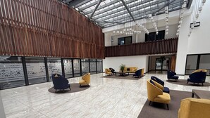 Un hall amplio con techo alto, mobiliario moderno y una gran pared de vidrio.