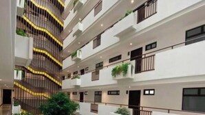 Un edificio de varios pisos con balcones, plantas de interior y un patio con zonas de estar.