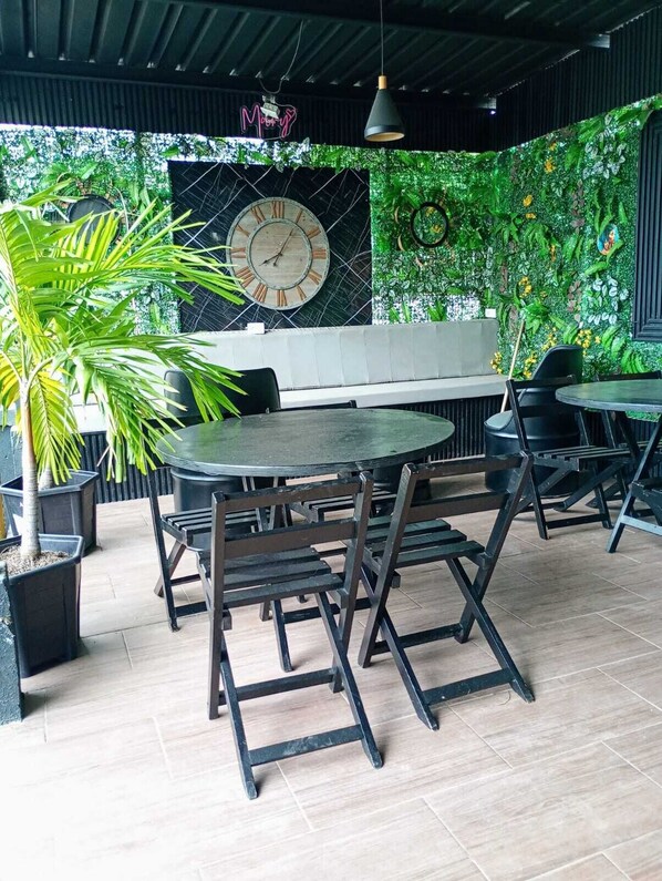 A restaurant with a round table and chairs, a clock on the wall, and a green wall with plants.