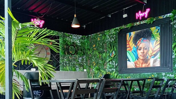An indoor dining area with a green wall, a neon sign, and a large screen displaying a colorful image. - Nice Apartment 5 (Cartagena de Indias)
