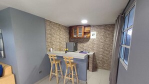 Eine kompakte Küche mit Bar, zwei Holzbarhocker, einem Kühlschrank und einem Fenster.