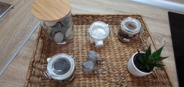 Un plateau en osier contenant quatre bocaux en verre, une paire de ciseaux et une plante en pot.