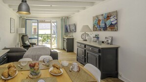 A cozy room with a dining table set for breakfast, a sofa, a TV, and a balcony with a view. - Le Cottage*Côte Sauvage*Plage*Shops*Parking (Le Croisic)