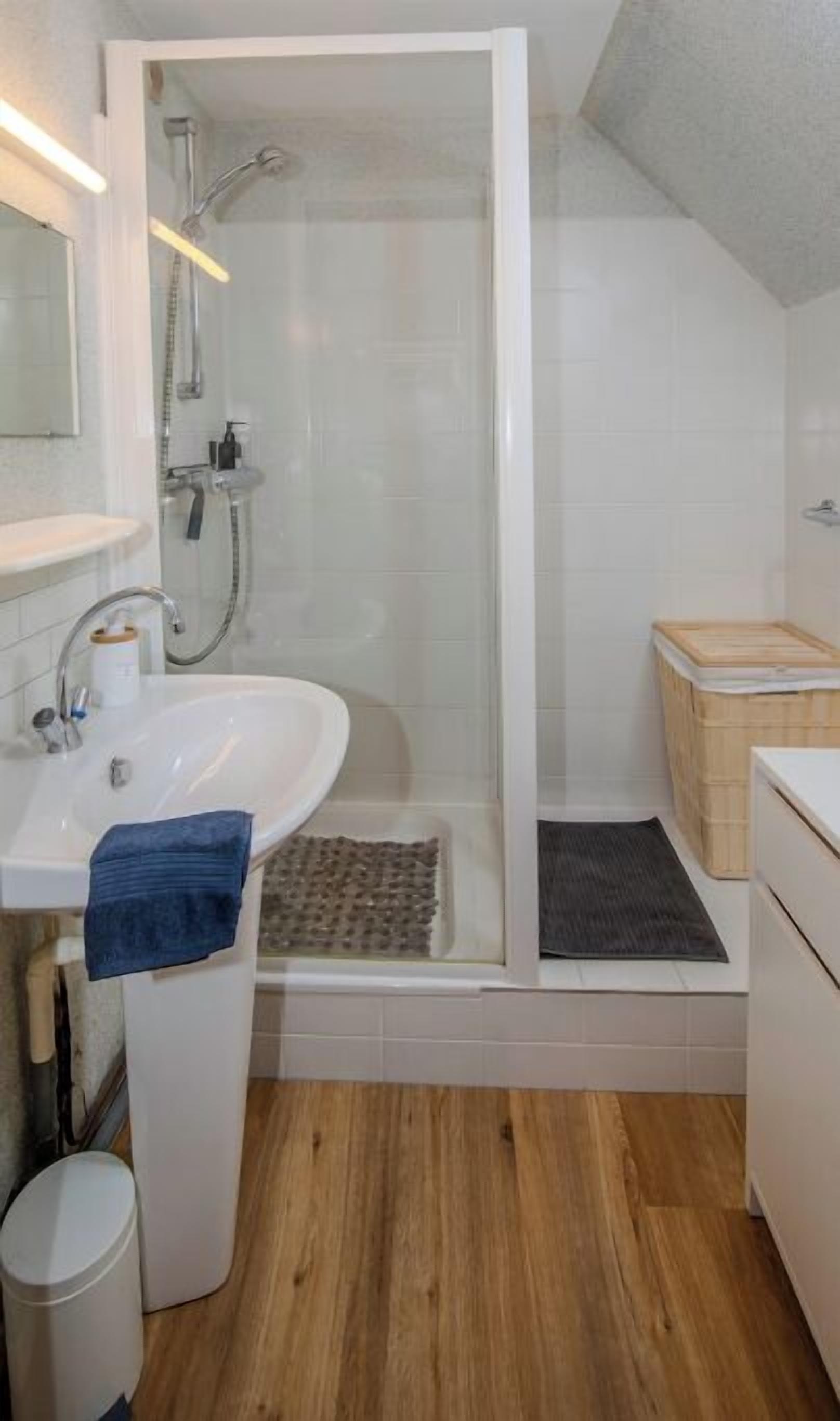 Een moderne badkamer met een wit wastafelmeubel, een douchecabine van glas en een houten vloer.