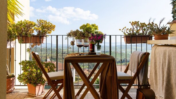 Un balcon avec deux chaises en bois, une petite table avec une bouteille et des verres, et des plantes en pot.