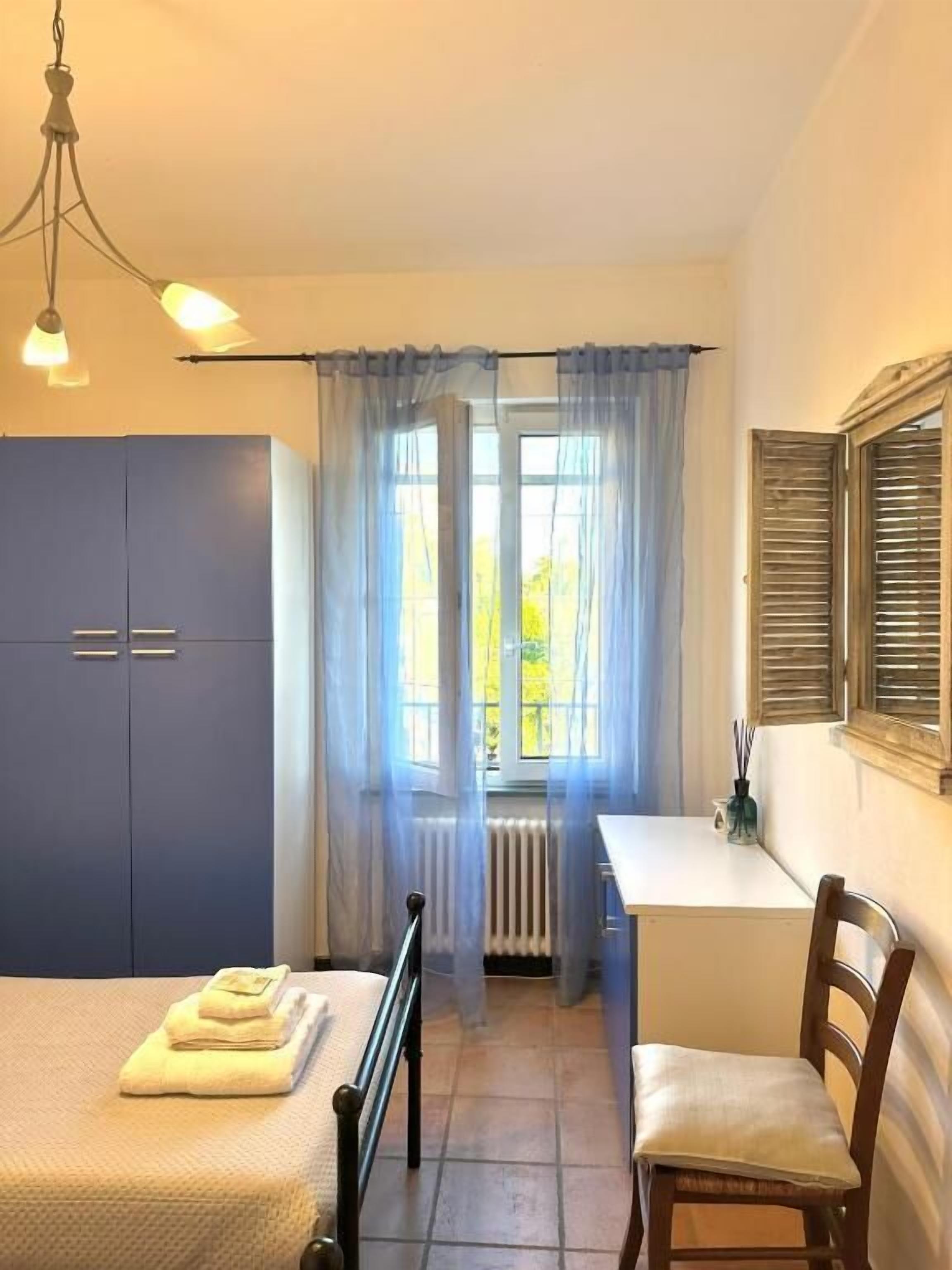 A bedroom with a bed, a chair, a desk, a radiator, and a window with curtains.