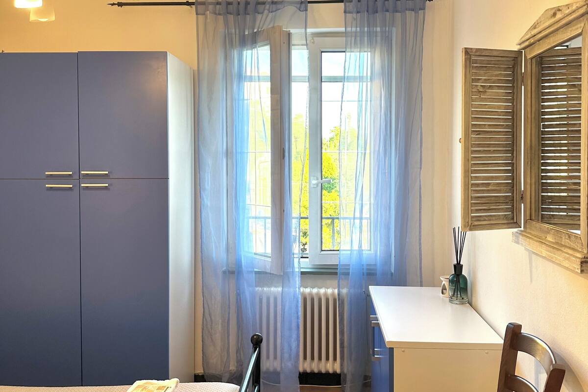 A bedroom with a bed, a desk, a chair, a wardrobe, and a window with curtains.