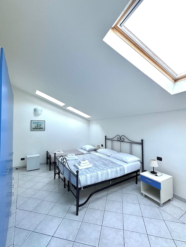 A bedroom with a skylight, a bed with a headboard, a bedside table with a lamp, and a small white cabinet. - Il Ciliegio (Vezzano Ligure)
