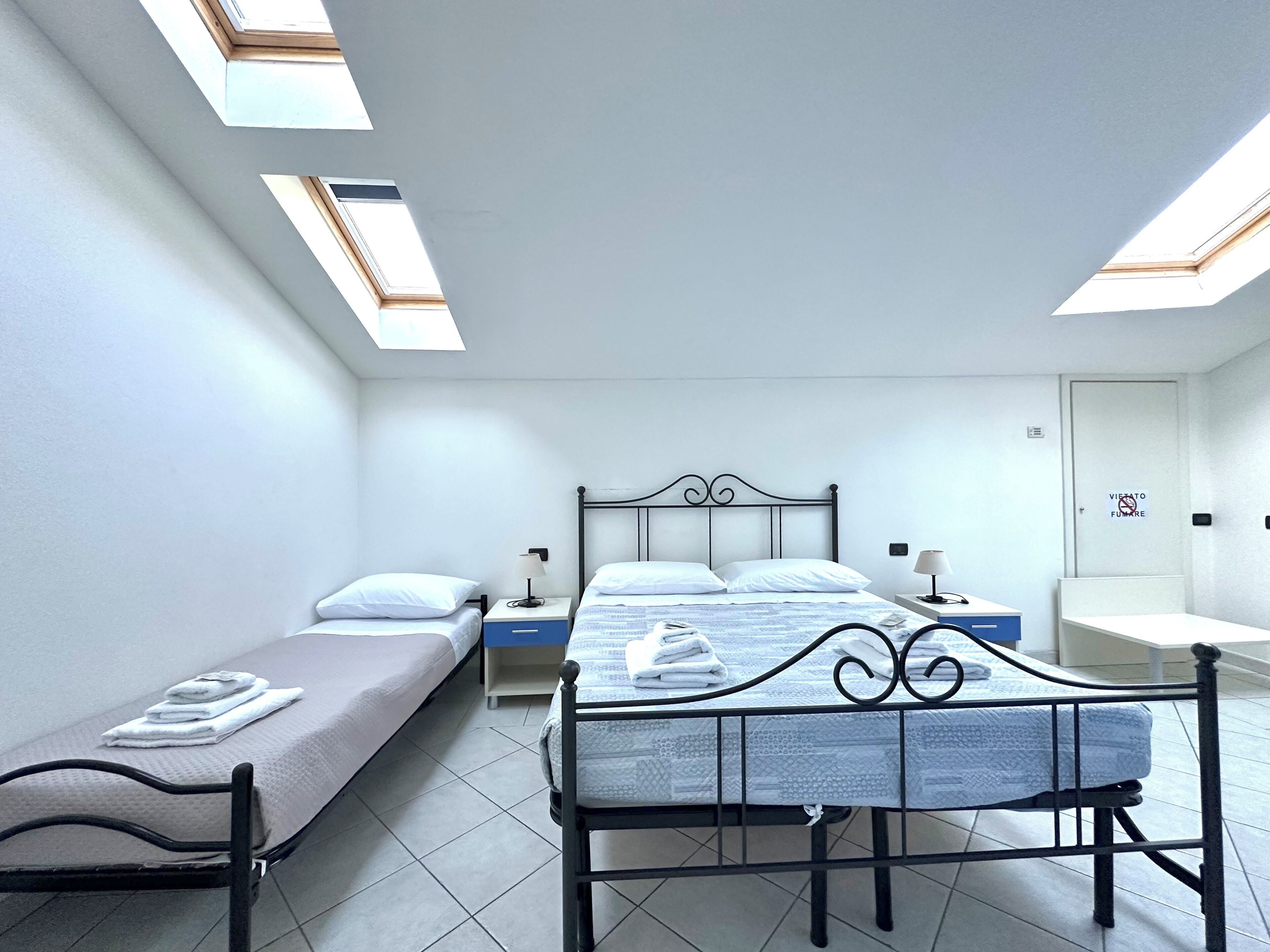 A room with two beds, a desk, and a chair. There are skylights on the ceiling.