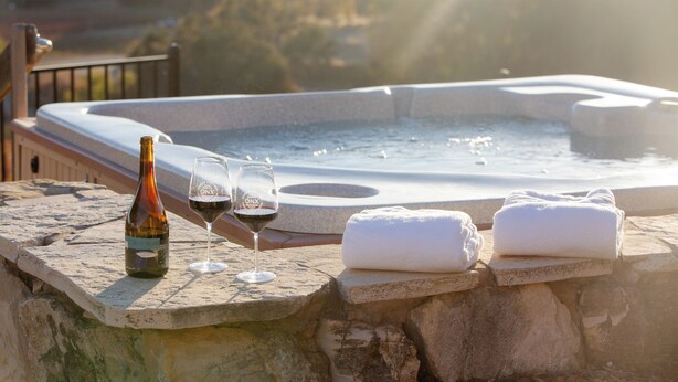 A hot tub with two glasses of wine and a bottle of wine on a stone ledge. - Kiler Ranch House is a charming 3-bedroom house that is ideal for a weekend away (Paso Robles)