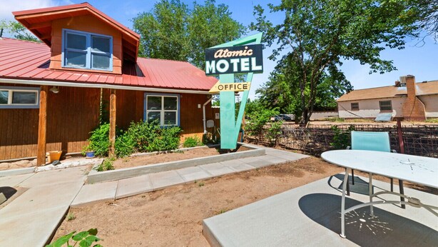 A wooden building with a red roof, a sign for the Atomic Motel Office, and a table with chairs in the foreground. - Atomic #2 I Downtown I Historic I Trailer Parking (Moab)