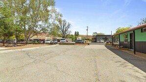 A parking lot with several cars, a building with a green facade, and trees in the background. - Atomic #2 I Downtown I Historic I Trailer Parking (Moab)