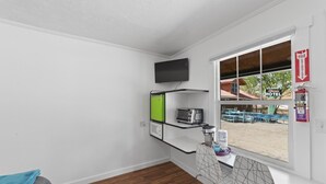 A room with a wooden floor, a window with a view of an outdoor area, a flat-screen TV mounted on the wall, and a small kitchenette with a toaster and a kettle. - Atomic #2 I Downtown I Historic I Trailer Parking (Moab)