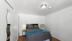 A bedroom with a bed, bedside table, lamp, and air conditioning unit. - Atomic #2 I Downtown I Historic I Trailer Parking (Moab)