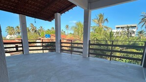 An open balcony with a concrete floor, wooden railing, and a view of palm trees and buildings. - Casa da Paz  (Trairi)