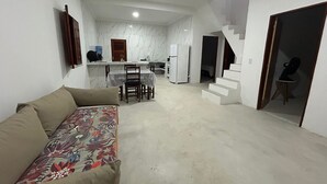 A living room with a sofa, a dining area with a table and chairs, a kitchen with a refrigerator, and a staircase leading to another level. - Casa da Paz  (Trairi)