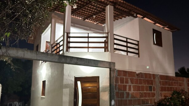 A two-story house with a balcony, a wooden door, and a brick wall. - Casa da Paz  (Trairi)