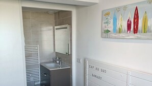 A modern bedroom with a bed, two pillows, a nightstand, a painting, and a bathroom visible through an open door. - Nice T2 on the little port of Sanary, Clim (Sanary-sur-Mer)