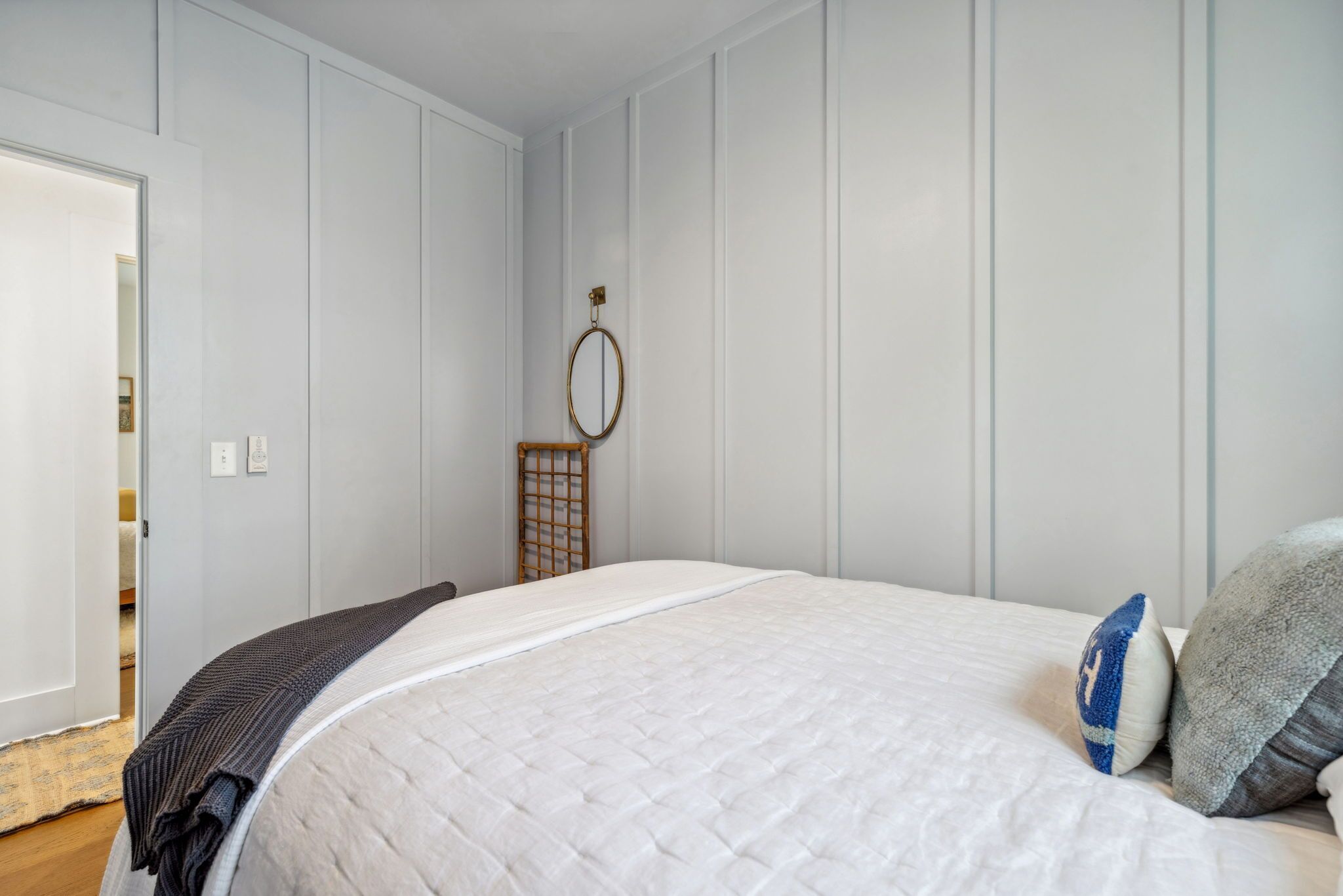 A bedroom with a large bed, a wooden headboard, a bedside table, and a wall-mounted mirror.