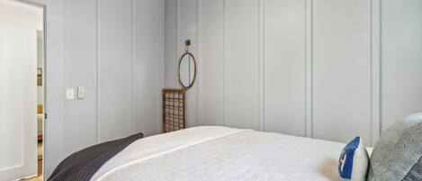 A bedroom with a large bed, a wooden headboard, a bedside table, and a wall-mounted mirror.