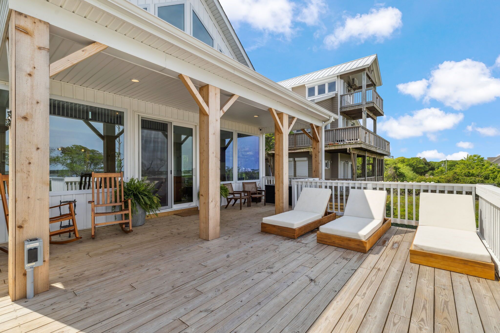A wooden deck with two lounge chairs, a rocking chair, and a table.