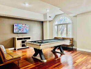 Relax in a spacious room with a pool table, comfortable sofa, and large window offering a view of the outdoors.