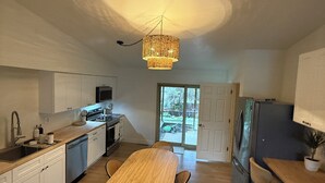 A compact kitchen with a wooden dining table, white cabinets, and a hanging light fixture. - Boho 3BR, 2BA Home in Colorado Springs Sleeps 6+ (Colorado Springs)