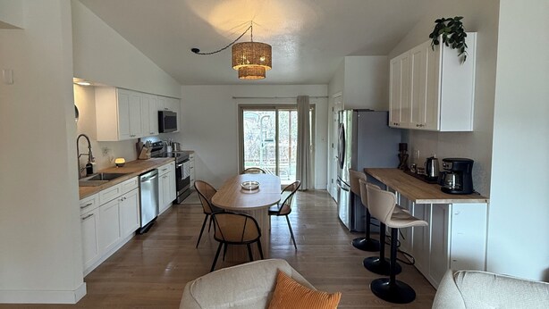 A modern kitchen with white cabinets, a dining area with a round table, and two armchairs with cushions. - Boho 3BR, 2BA Home in Colorado Springs Sleeps 6+ (Colorado Springs)