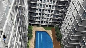 A high-rise residential building with a central swimming pool surrounded by greenery and a paved walkway. - Glamorous 2BR/1Bath/Wifi/Netflix/Heater/Washing/5starBnB (Pasay)
