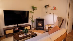 A living room with a flat-screen TV, a sofa, a coffee table, a fireplace, and a bookshelf. - Wellness Retreat at Lake Cushman. Sauna, Cold Plunge, Fire Pit (Hoodsport)
