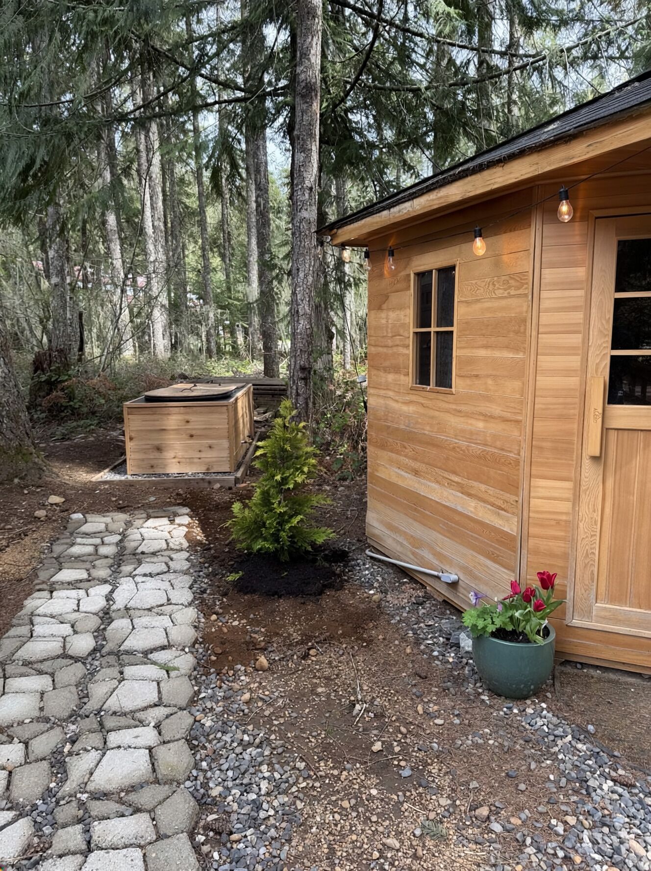 Een houten chalet met een pad van stenen, een kleine tuin en een houten tuinhuis.