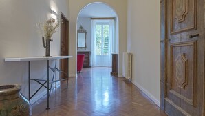 Un pasillo con piso de madera, una mesa blanca con un florero y una puerta grande de madera.