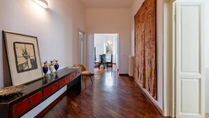 A hallway with a wooden floor, a dark wooden console table with red drawers, a framed picture, and a tapestry on the wall. - Modern, Bright and Spacious 2-Bedroom Apartment (Firenze)