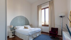 A bedroom with a bed, a chair, a lamp, and a window. - Modern, Bright and Spacious 2-Bedroom Apartment (Firenze)