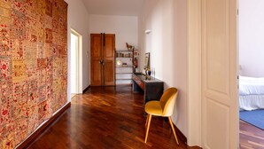 A room with a wooden floor, a yellow chair, a desk with a lamp, and a bed with white bedding. - Modern, Bright and Spacious 2-Bedroom Apartment (Firenze)