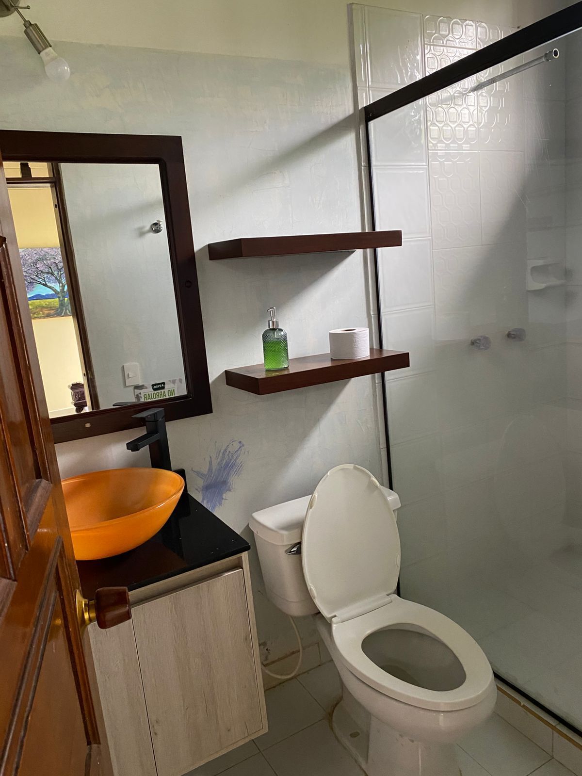 A bathroom with a wooden vanity, a white toilet, a glass bowl sink, and a shower enclosure.