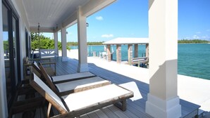 A covered outdoor area with wooden lounge chairs and a view of the water.