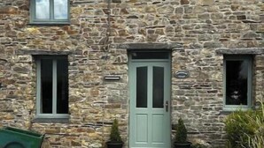Un bâtiment en pierre avec une porte verte, deux fenêtres et une petite brouette.