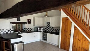 Une cuisine avec des meubles blancs, un plan de travail noir, un réfrigérateur en acier inoxydable et un escalier en bois.