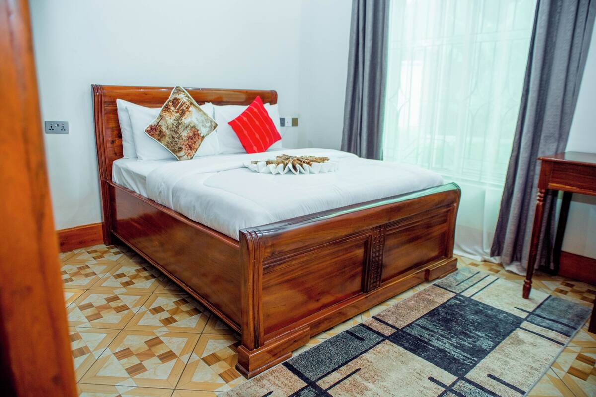 Uma cama bem arrumada com cabeceira de madeira, um tapete estampado e uma mesinha de cabeceira.