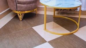 Un sillón tapizado con marco dorado, una mesita de mármol con base dorada y un suelo a cuadros.