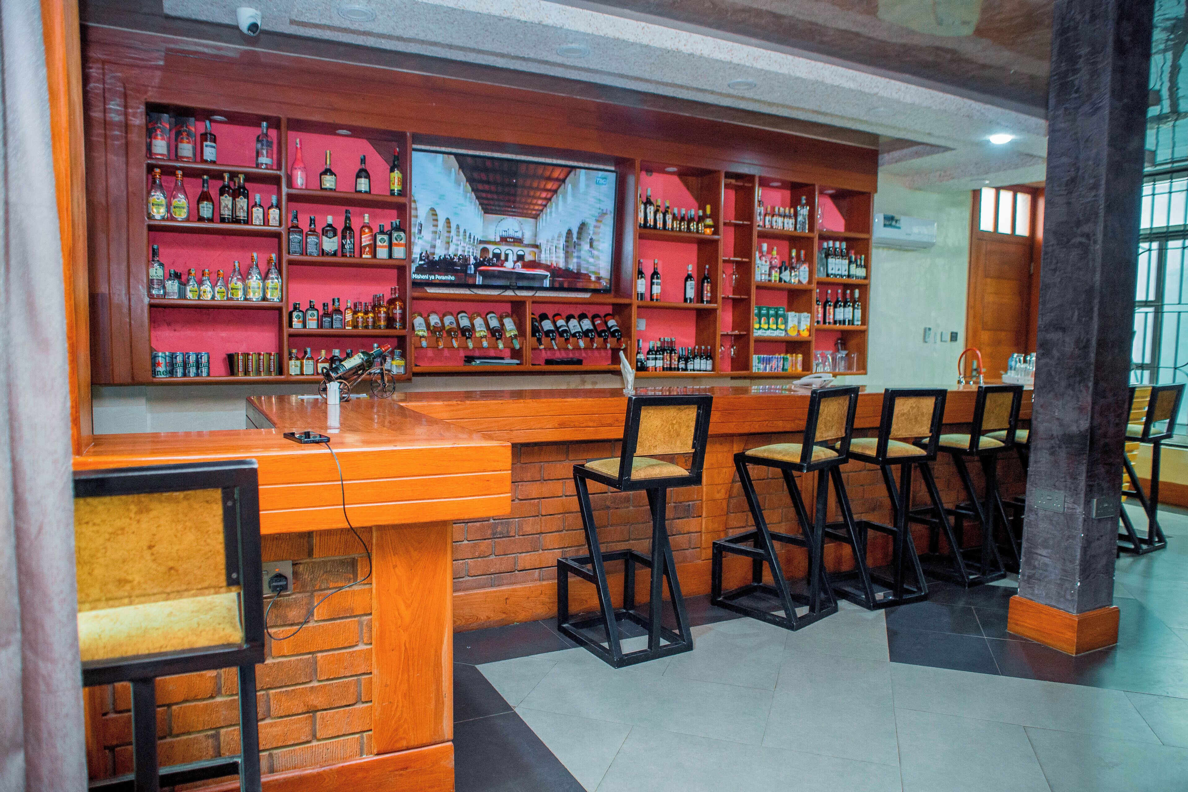 Zona de bar con televisor, estantes llenos de botellas y taburetes.