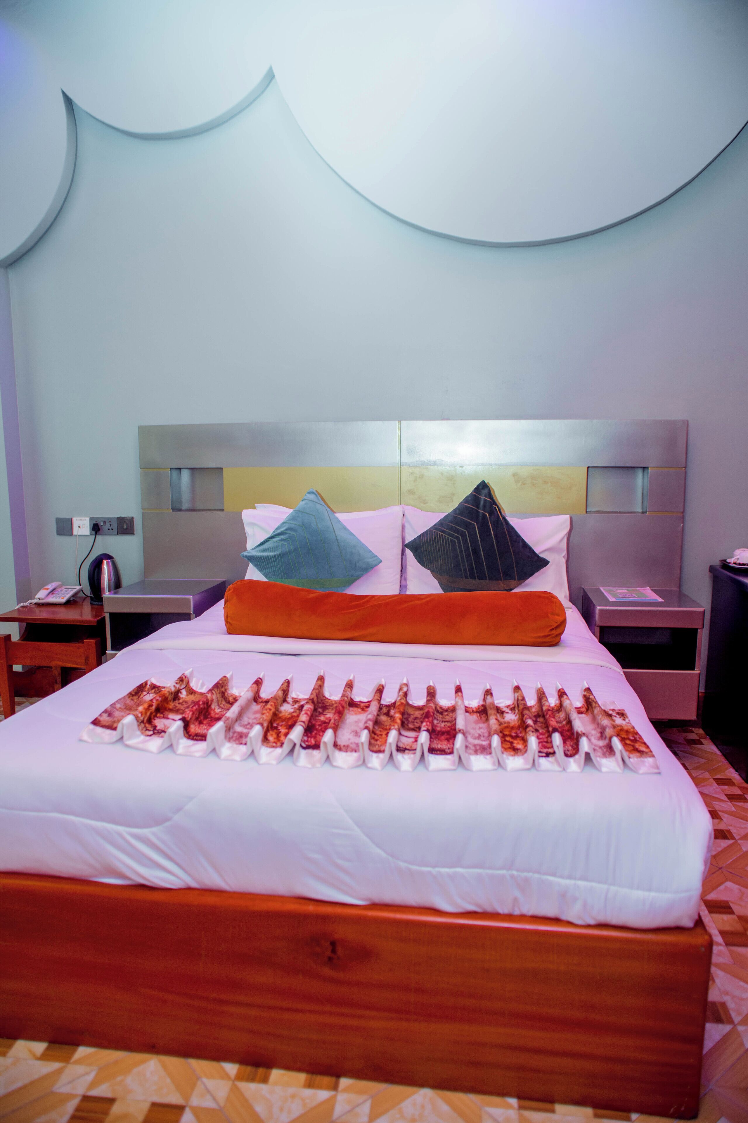 A hotel room with a large bed, a wooden headboard, and a bedside table with a lamp.