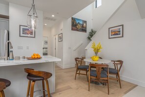 A modern kitchen with a white island, bar stools, and a dining area with wooden chairs and a round table. - Modern Mountain Living Near Donner Lake (Truckee)