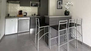 Una cocina moderna con lavavajillas, microondas y una pequeña zona de comedor con sillas de metal y una mesa.