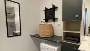 Un lavadero con lavadora, un espejo y estantes con ropa doblada y una cesta tejida.